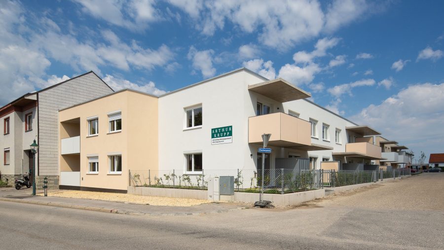 Moderne Wohngebäude an einer Straßenecke bei blauem Himmel.
