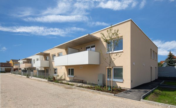 Moderne Wohngebäude mit Balkonen, hellbeige Fassade, sonniger Himmel und gepflegte Umgebung.