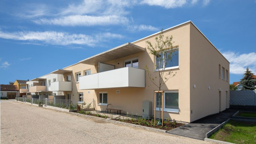 Moderne Wohngebäude mit Balkonen, hellbeige Fassade, sonniger Himmel und gepflegte Umgebung.