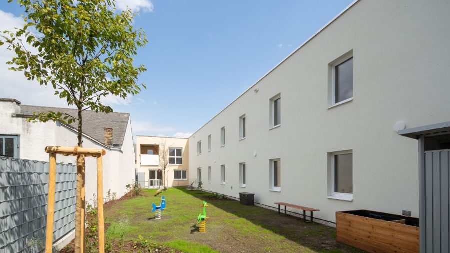 Moderner Hinterhof mit Garten und Spielplatz an einem Gebäude bei sonnigem Wetter.