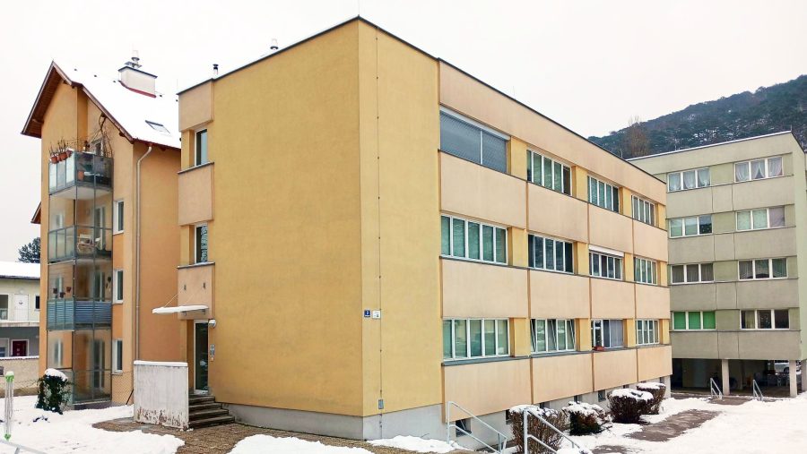 Gelbes Wohngebäude im Winter mit schneebedecktem Boden und Hintergrund.