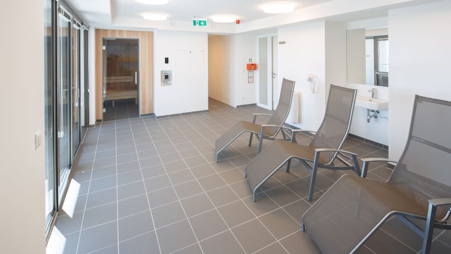 Moderner Wellnessbereich mit Liegestühlen und großen Fenstern in einem minimalistischen Design.