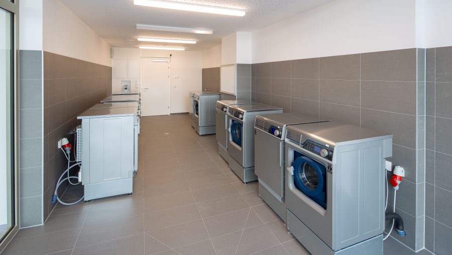 Moderner Waschraum mit mehreren Waschmaschinen an grauen Fliesenwänden.