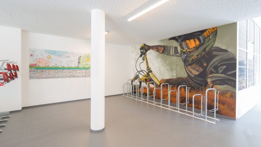 Innenansicht mit Wandgemälde eines Radfahrers und Kinderzeichnung, Fahrradständer im Vordergrund.