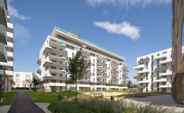 Moderne Wohnanlage mit Grünflächen und Spielplatz unter blauem Himmel.