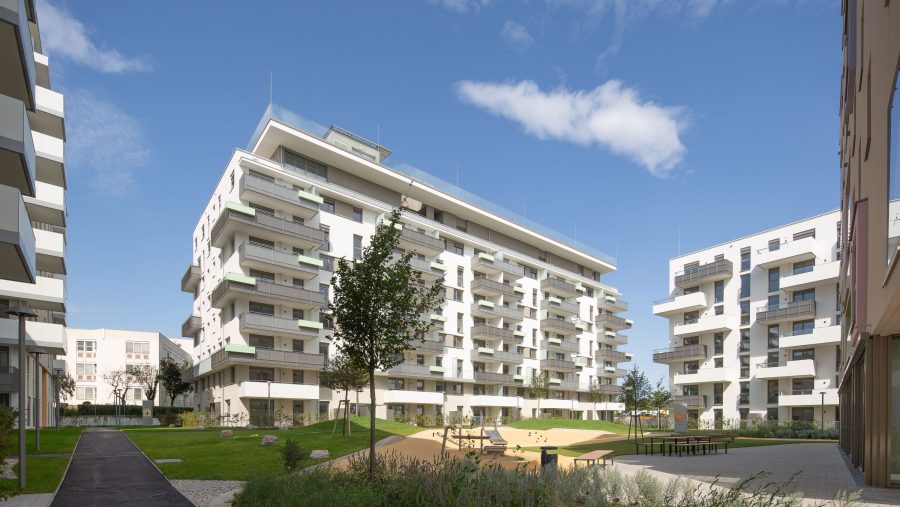 Moderne Wohnanlage mit Grünflächen und Spielplatz unter blauem Himmel.