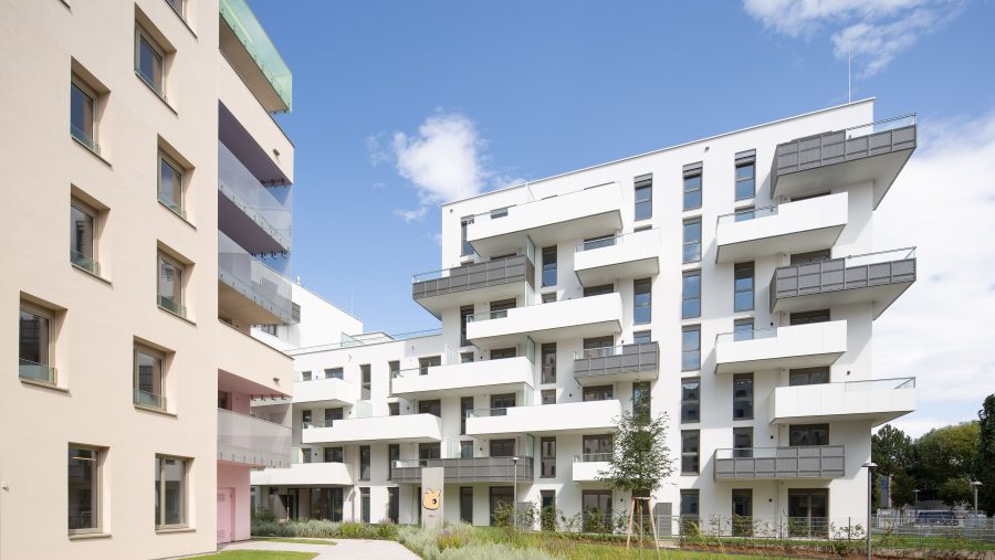 Moderne Wohngebäude mit Balkonen vor blauem Himmel, grüner Garten im Vordergrund.