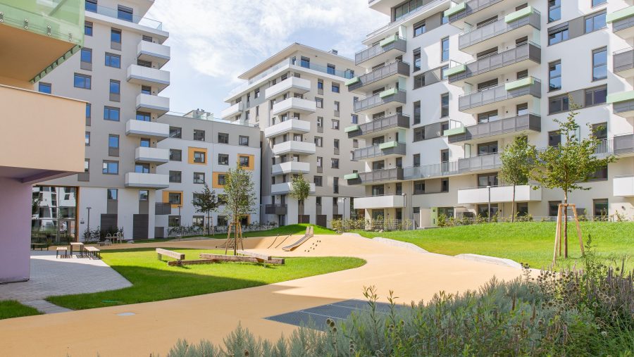 Moderne Wohnanlage mit Spielplatz und Grünfläche an einem sonnigen Tag.