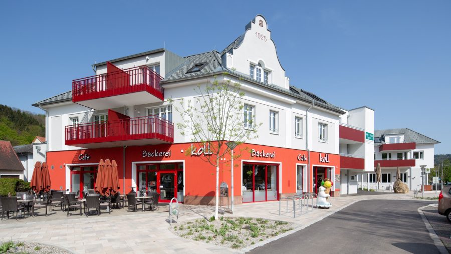 Moderne Bäckerei mit Café und Außensitzbereich an sonnigem Tag in städtischer Umgebung.