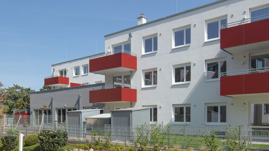 Moderne Wohnanlage mit roten Balkonen und weißen Fassaden an einem sonnigen Tag.