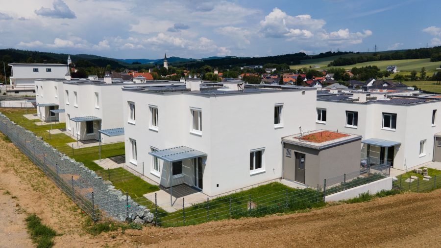 Reihenhäuser in einer ländlichen Gegend mit grünem Rasen und bewölktem Himmel.