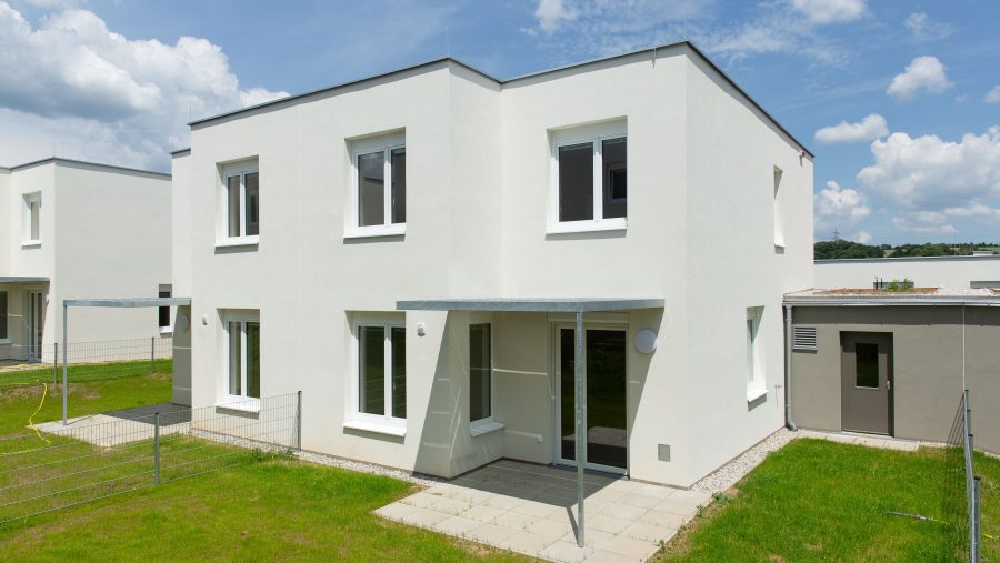 Modernes weißes Wohnhaus mit Garten an einem sonnigen Tag.