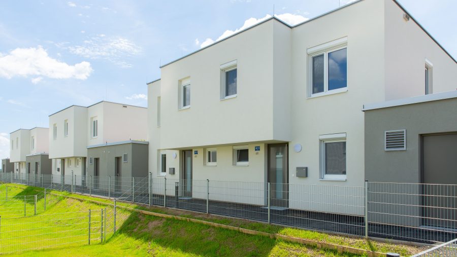 Moderne Reihenhäuser mit weißen Fassaden und Zäunen an einem sonnigen Tag.