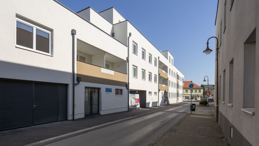 Moderne Wohngebäude an einer Straße an einem sonnigen Tag, mit klarer blauer Himmel im Hintergrund.