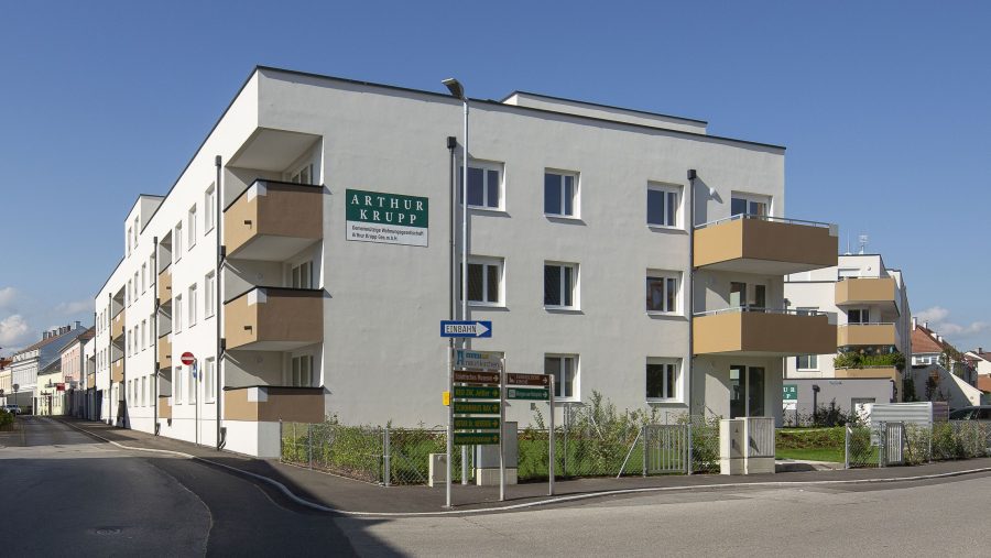 Mehrfamilienhaus an einer Straßenecke mit blauer Himmel im Hintergrund.
