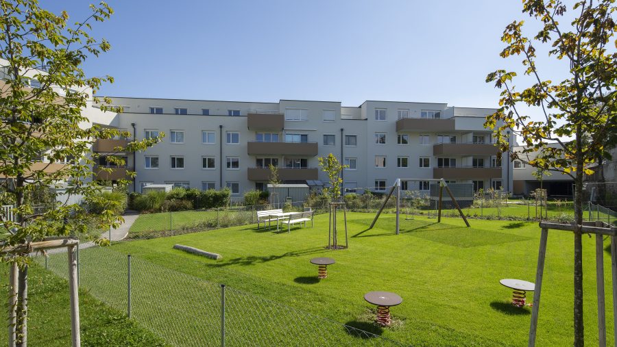 Mehrfamilienhaus mit grünem Innenhof und Spielplatz, sonniger Tag.