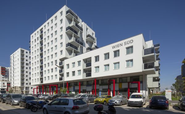 Moderne Wohngebäude in Stadtumgebung bei Sonnenschein, mit geparkten Autos im Vordergrund.