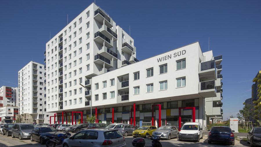 Moderne Wohngebäude in Stadtumgebung bei Sonnenschein, mit geparkten Autos im Vordergrund.