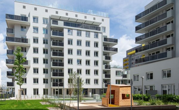 Mehrstöckiges Wohngebäude mit modernem Design und grünem Innenhof an einem sonnigen Tag.