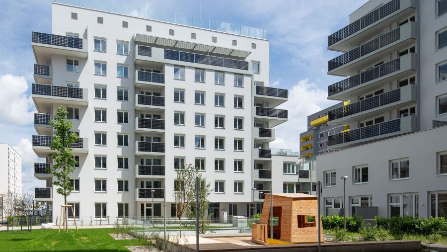 Mehrstöckiges Wohngebäude mit modernem Design und grünem Innenhof an einem sonnigen Tag.