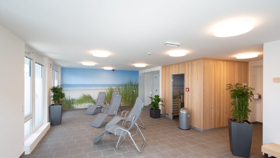 Moderner Ruheraum mit Liegestühlen und Wandbild eines Strandes, helle Beleuchtung und Holzverkleidung.