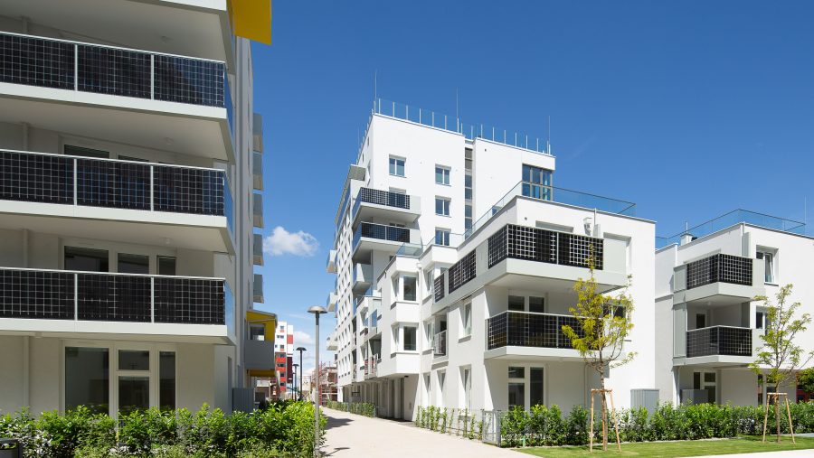 Moderne Wohngebäude bei sonnigem Wetter in einem Stadtviertel, mit klaren blauen Himmel im Hintergrund.