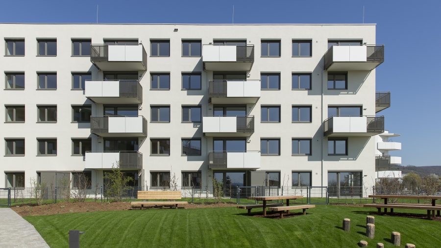 Moderne Wohnanlage mit Balkonen, blauer Himmel im Hintergrund, gepflegter Rasen im Vordergrund.