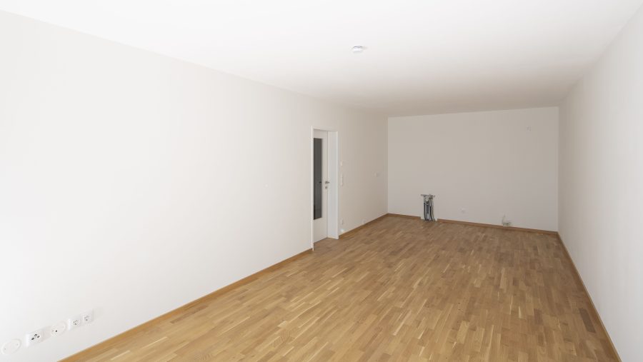 Leerer Raum mit Holzfußboden und weißer Wand, bereit zur Gestaltung.