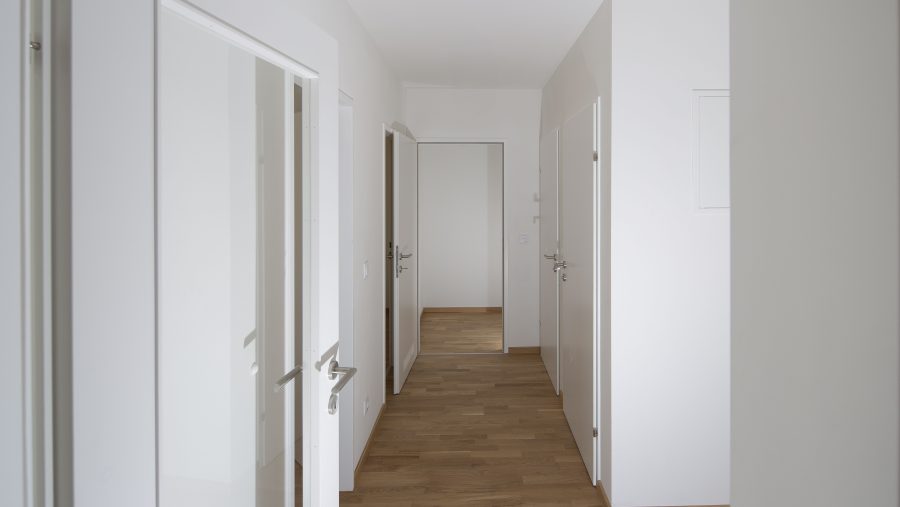 Moderner Flur mit Holzboden und weißen Türen in einer Wohnung.
