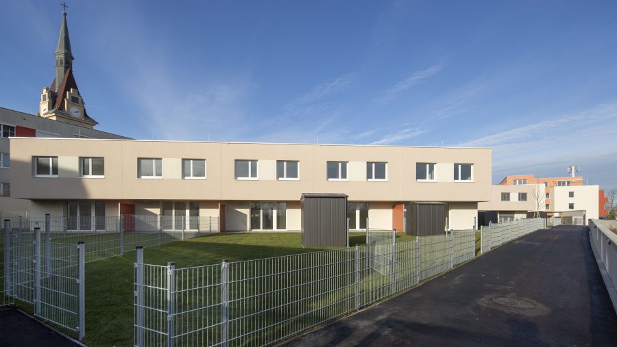 Moderne Wohngebäude mit Rasenfläche und Zaun bei blauem Himmel.