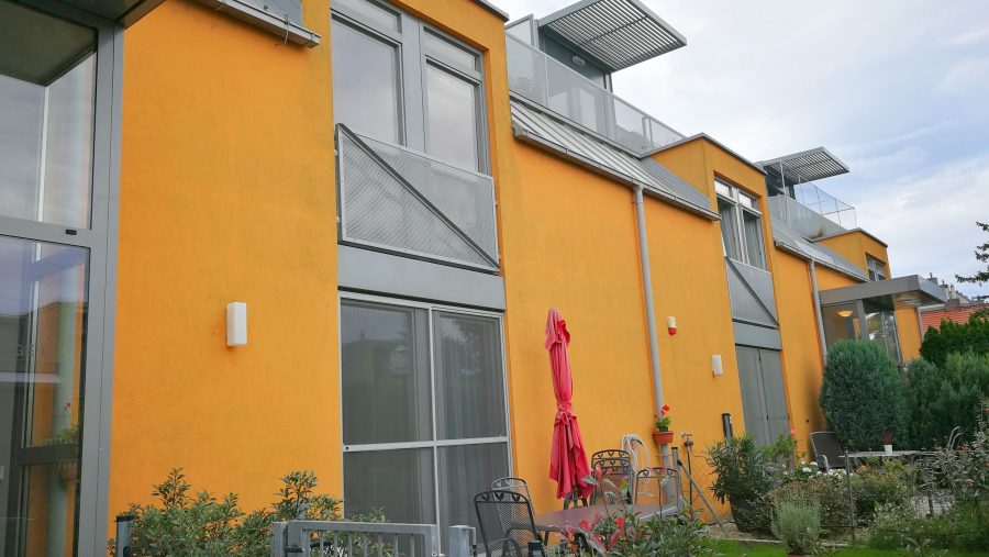 Moderne gelbes Wohngebäude mit Garten und Terrasse, Fokus auf Architektur und Außenbereich.