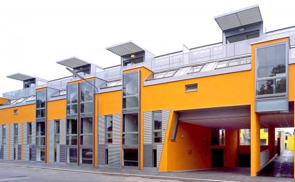 Moderne Architektur: Mehrfamilienhaus mit leuchtend gelber Fassade und großen Fenstern.
