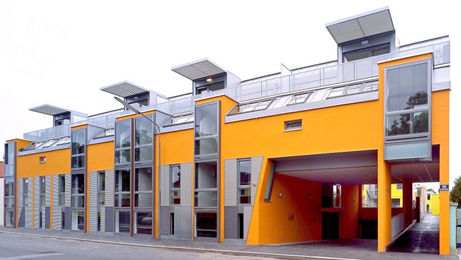 Moderne Architektur: Mehrfamilienhaus mit leuchtend gelber Fassade und großen Fenstern.