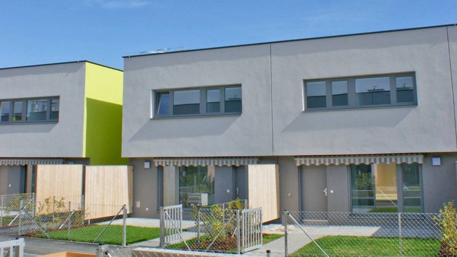 Moderne Reihenhäuser mit Garten und hellem Anstrich unter blauem Himmel.