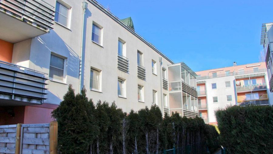 Moderne Wohnanlage mit Balkonen und grüner Hecke unter blauem Himmel. Perfekt für Wohnungskauf in ruhiger Lage.