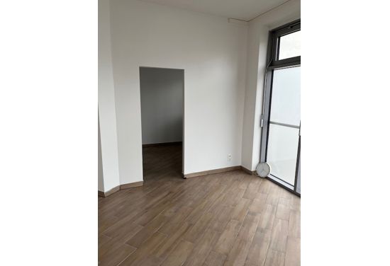 Leerer Raum mit Holzboden, offenem Türbereich und großer Fensterfront für viel Tageslicht.