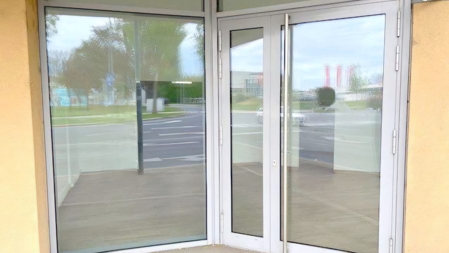 Glas-Eingangstür eines leeren Geschäftsraums mit Blick auf die Straße und Bäumen im Hintergrund.