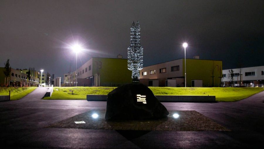 Nachtaufnahme eines modernen Gebäudekomplexes mit beleuchteter Skulptur im Vordergrund.