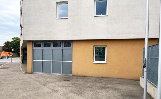 Modernes Gebäude mit gelbem und grauem Anstrich und Glasfenstern, draußen eine leere Einfahrt bei bewölktem Himmel.