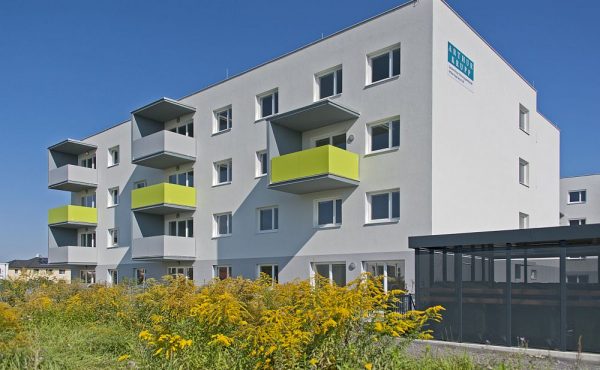 Moderne Wohnanlage mit Balkonen und Gartenanlage im Vordergrund unter klarem blauem Himmel.