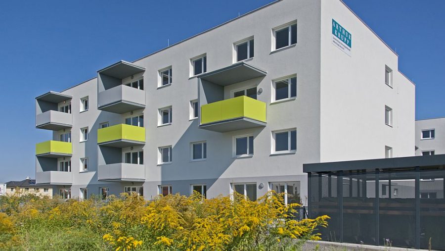 Moderne Wohnanlage mit Balkonen und Gartenanlage im Vordergrund unter klarem blauem Himmel.
