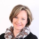 Eine lächelnde Frau mit Schal, die professionell für Immobilienberatung auftritt.