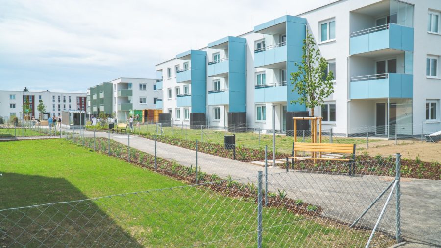 Moderne Wohnanlagen mit Grünflächen und Gehwegen an einem sonnigen Tag.