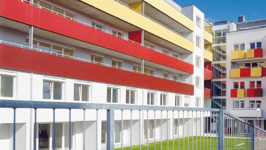 Modernes Gebäude mit farbigen Fassaden und Balkonen, blauer Himmel im Hintergrund.