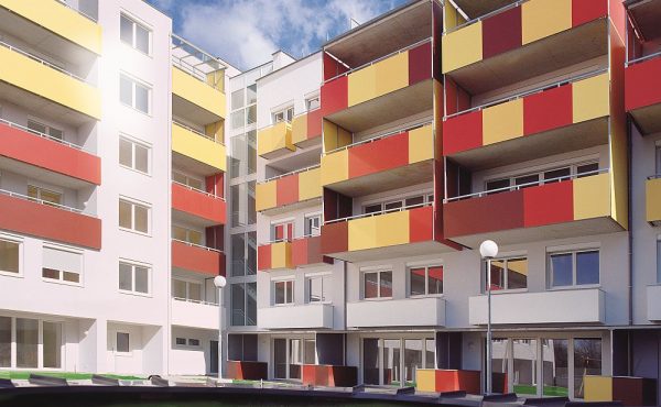 Moderne Wohngebäude mit bunten Balkonen und grünem Innenhof bei sonnigem Wetter.