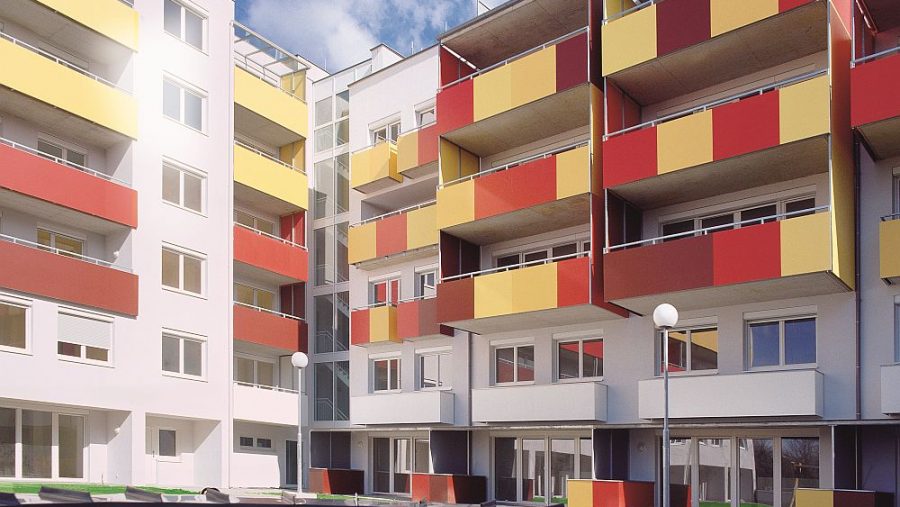 Moderne Wohngebäude mit bunten Balkonen und grünem Innenhof bei sonnigem Wetter.