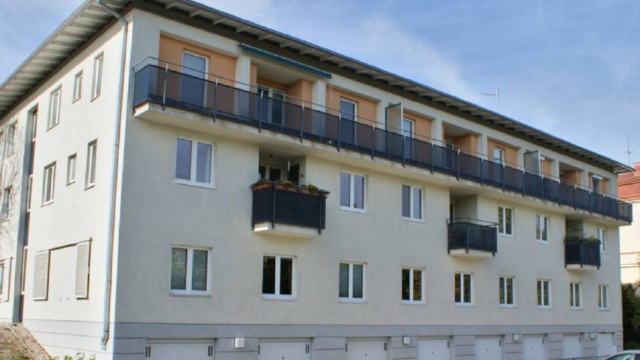 Mehrstöckiges Wohngebäude mit Balkonen und Parkplätzen an einem sonnigen Tag.