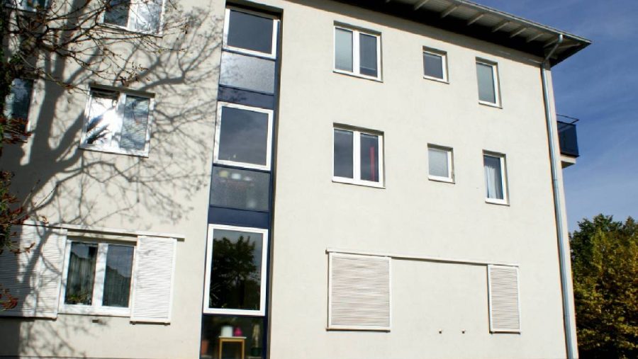 Mehrfamilienhaus mit weißen Wänden und Fenstern im Sonnenschein.