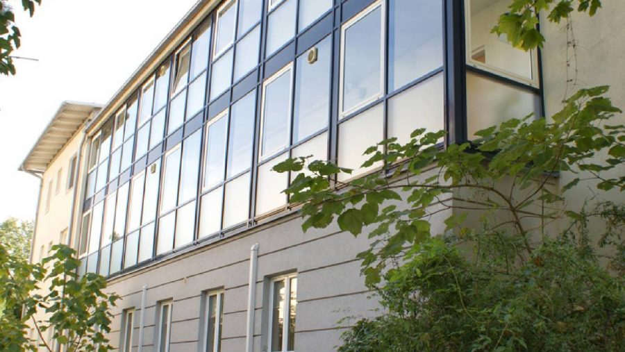 Gebäude mit verglaster Fassade und umgebender Vegetation, von unten betrachtet.