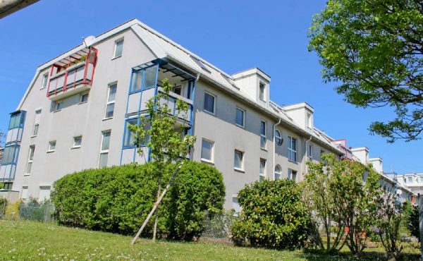 Modernes Wohngebäude mit grüner Umgebung und klarer Himmel im Hintergrund.